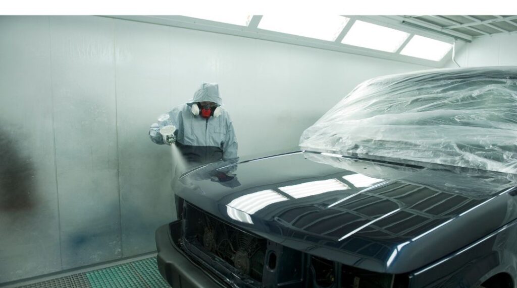 Technician in protective gear spray painting a car in an auto body paint and refinishing shop.