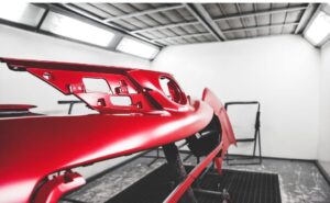 Freshly painted red car bumper in a professional auto body shop.